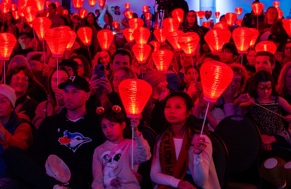 Une foule de personnes assises, brandissant des lanternes rouges, lors d'un événement Illuminons la nuit.