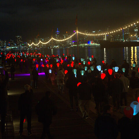 Un grand groupe de personnes marchant la nuit avec des lanternes allumées près d'un quai d'eau