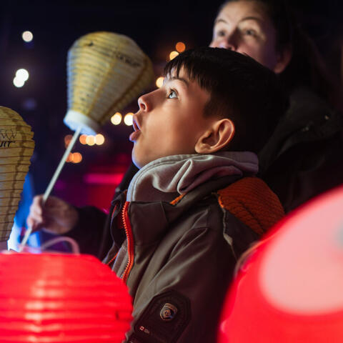 Un jeune garçon et une femme avec des expressions choquées, tenant des lanternes et regardant quelque chose hors caméra